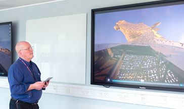 A Ӱֱstaff member standing by 2 screens showing the Scottish Kelpies sculpture