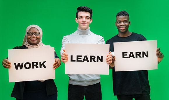 Three Ӱֱ students holding signs with the words "Work", "Learn" and "Earn"