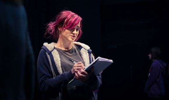 A Ӱֱstage management student reading and making notes on a notepad on stage