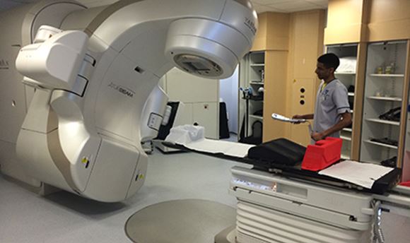 A Ӱֱstudent standing beside a Radiotherapy machine