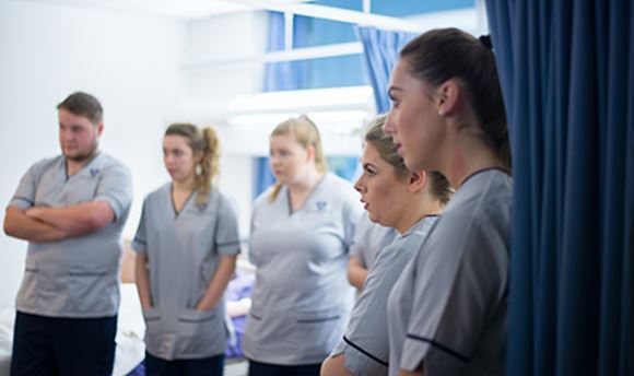 A row of Ӱֱstudent nurses listening intently as a senior nurse speaks to them